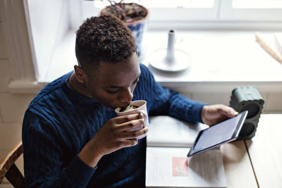 High angle view of teenage boy drinking black coffee while e-learning using digital tablet at home