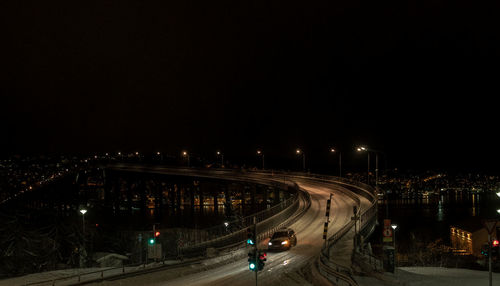 Vehicles on illuminated road against sky at night