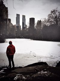 Rear view of man standing by frozen lake in city
