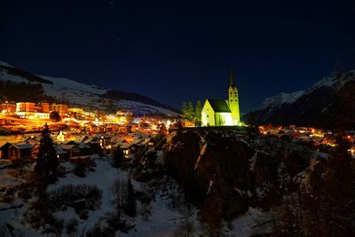 Illuminated buildings in city against sky at night during winter