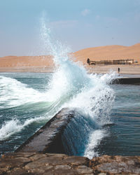 Waves splashing on shore against sky