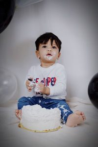 Cute baby boy eating birthday cake while sitting at home