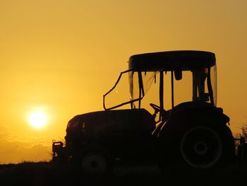 Silhouette machinery on field against sky during sunset