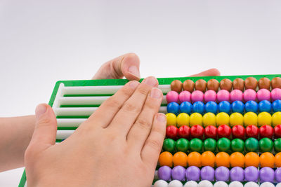 Cropped hands of child holding abacus against white background