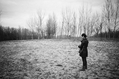 Woman standing on field with bare trees against sky