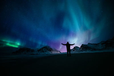 Rear view of silhouette person standing on field against sky at night