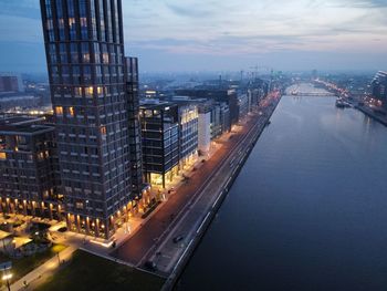 High angle view of illuminated buildings by river against sky