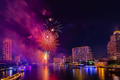 Firework display over river by buildings against sky at night