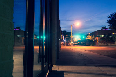 Illuminated street amidst buildings against sky at night