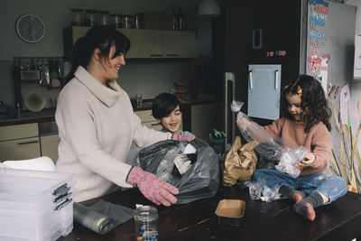 Smiling mother with son and daughter collecting plastic bags at home