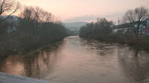 River amidst bare trees against sky during sunset