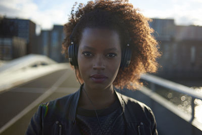 Portrait of confident woman listening music while standing on bridge