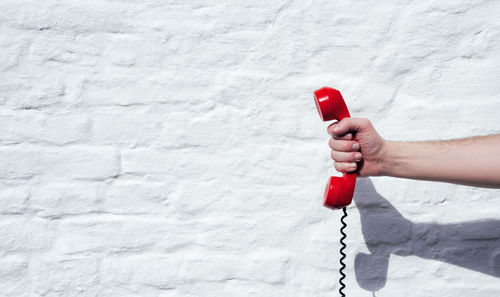 Midsection of person holding red umbrella against wall