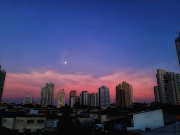 Buildings in city against romantic sky at sunset