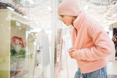 Girl in pink clothes with a backpack looks at a showcase with flowers shopping day