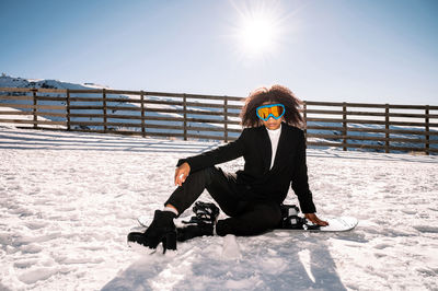 Man sitting on snow against sky during sunny day