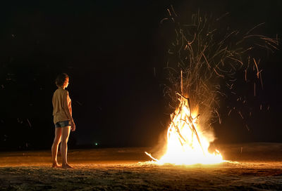 Full length of woman looking at bonfire at beach during night