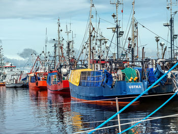 Fishing boats moored at harbor against sky