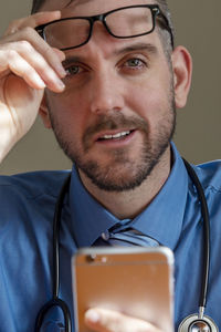 Doctor using smart phone raising reading glasses holding smart phone.