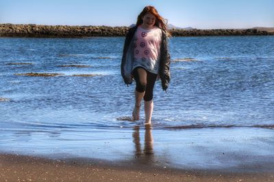 Full length portrait of young woman standing at beach