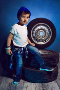 Boy in a white t shirt shirt and hat sits on a background of car wheels on a blue