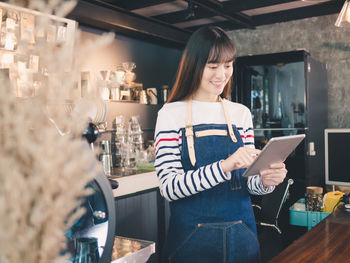 Midsection of woman holding smart phone while standing in cafe