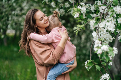 Young mother with her daughter in her arms in a blooming apple orchard