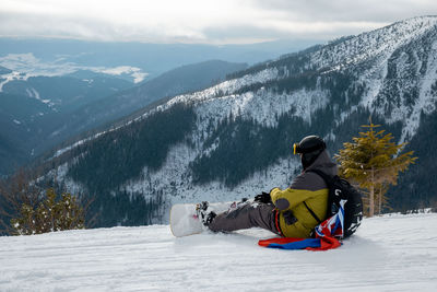 Rear view of man sitting on snowcapped mountain