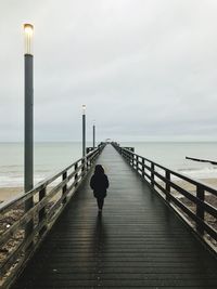 Rear view of man on pier over sea against sky