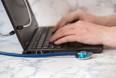 Stethoscope and the black notebook with human fingers on the table