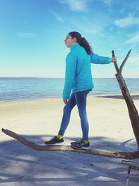 Side view of girl looking away while standing on branch at beach against sky