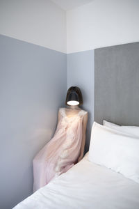 Woman with lamp in front of her face sitting by bed