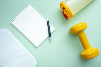 Weighing scale, yellow dumbbells, water bottle and notebook on green background. weight management.