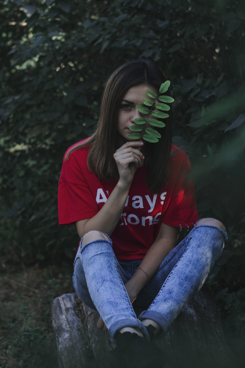 PORTRAIT OF A YOUNG WOMAN SITTING ON A LAND