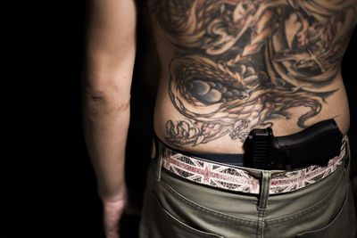 Midsection of tattooed man with gun in darkroom