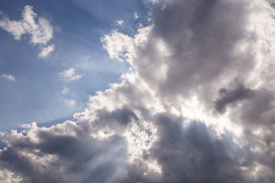 Low angle view of sunlight streaming through clouds