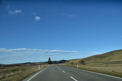 Country road along landscape against blue sky