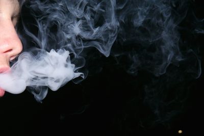 Cropped image of man smoking against black background