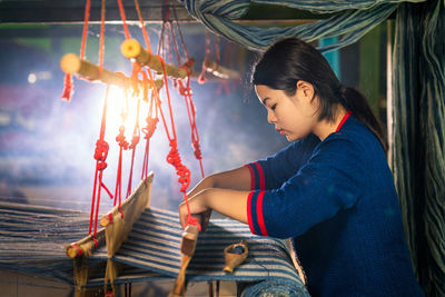 Side view of woman weaving loom in workshop