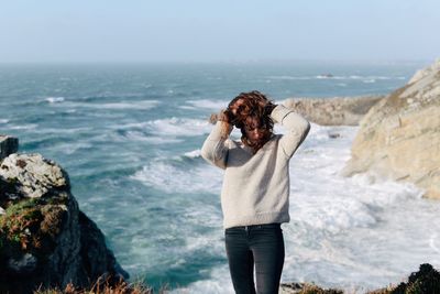 Young woman with hands in hair standing against sea