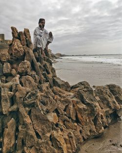 Man statue on rock at beach against sky