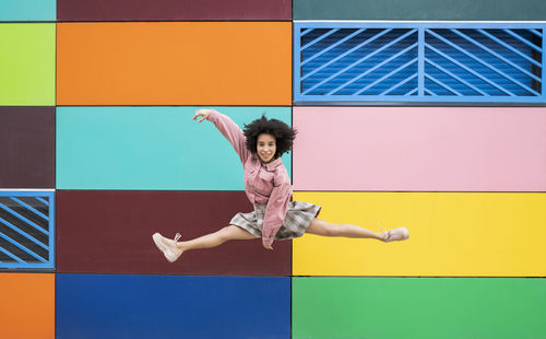 Female dancer jumping with leg splits in front of multi colored wall