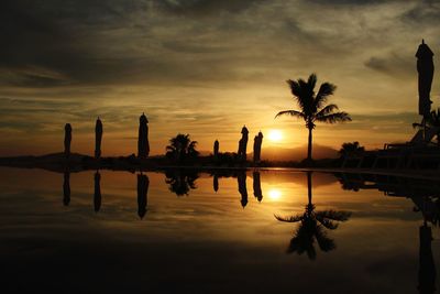 Silhouette palm trees by swimming pool against sky during sunset