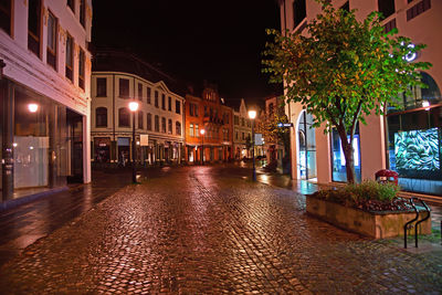 Illuminated street amidst buildings at night