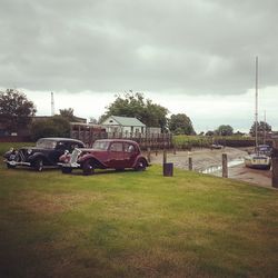 Cars parked on field against cloudy sky