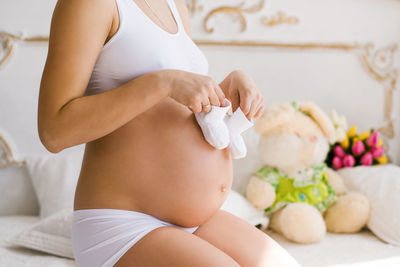 A pregnant woman holds white booties in her hands. a young woman for pregnant women