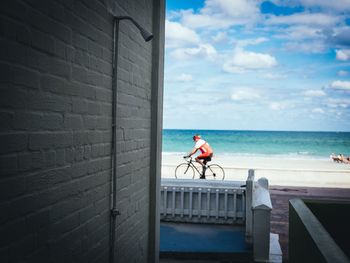 Man with bicycle by sea against sky