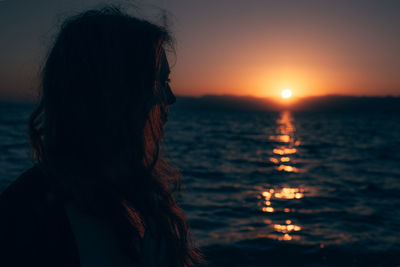 Side view of woman looking at sea against sky during sunset