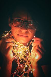 Close-up of girl with illuminated lighting equipment against black background