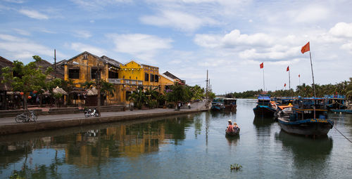 Boats in river by buildings in city against sky